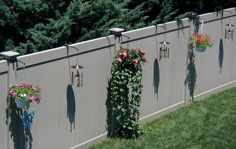 Plants of different heights ang lights at intervals along fence - nice Vinyl Fence Decor, Hanging Plants On Fence, Vinyl Fence Landscaping, Fence Hangers, Fence Hanging Planters, Chainlink Fence, Backyard Fence Decor, Fence Decorations, Vinyl Privacy Fence