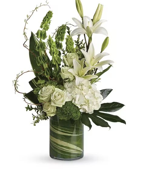 A modern accent for any occasion, this beautiful botanical sculpture blends snow white hydrangea and lilies with unique greens for a peaceful, Eastern-inspired feel. This modern bouquet includes white hydrangea, green roses, white Asiatic lilies, green trick dianthus, bells of Ireland, green button spray chrysanthemums, curly willow, Oregonia, variegated aspidistra leaves, small aralia leaf, green ti leaf, and lemon leaf. #WelkesFlorist Beauty Bouquet, Display Visual Merchandising, Greenery Design, Modern Bouquet, Get Well Flowers, Asiatic Lilies, Anniversary Flowers, Modern Flower Arrangements, Order Flowers Online