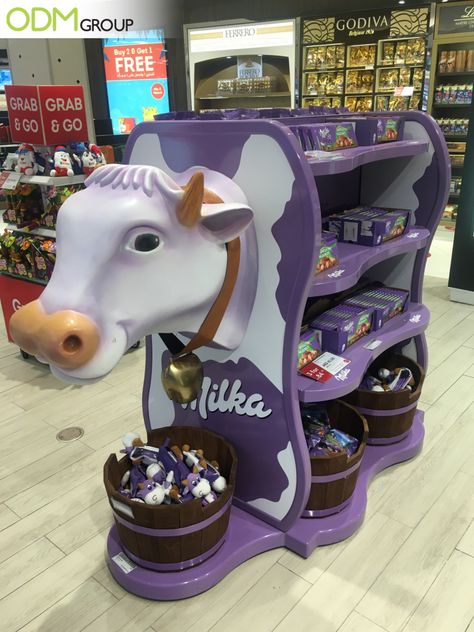 What brand comes to mind when you see a purple cow display inside the store? We automatically associate it with the chocolate brand Milka, correct? One of our staff members has recently come across their retail marketing display at a Duty-Free shop. The signature purple display is a head-turner! #POS #display #unique #eyecatching #catchy #design Milk Display, Retail Display Design, Toy Shop Display, Display Shelf Design, Duty Free Shop, Shopper Marketing, Retail Design Display, Grocery Store Design, Retail Marketing