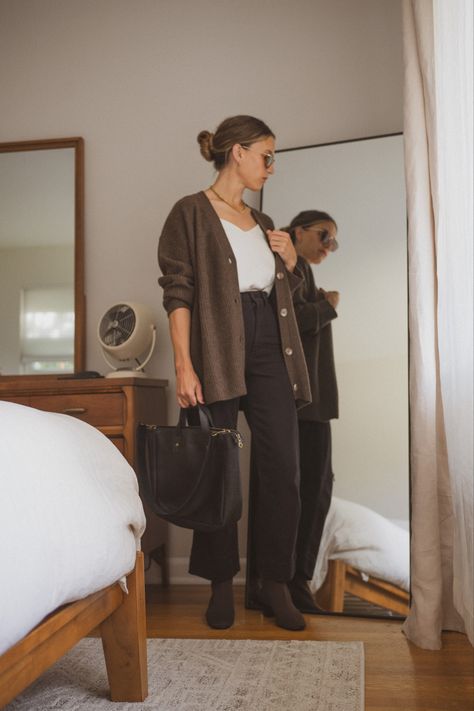 Ashley in her bedroom next to a bed and vintage dresser wearing a white silk cami, chocolate brown oversized cardigan, black cropped pants, brown sock booties, tortoiseshell sunglasses, and a black tote bag Styling Brown Cardigan, Brown Button Up Cardigan Outfit, How To Style A Brown Cardigan, Chocolate Brown Cardigan Outfit, Cardigan Button Up Outfit, Black Cardigan Outfit Spring, Black Outfit Brown Boots, Outfits With Brown Cardigan, Brown Boots With Black Pants