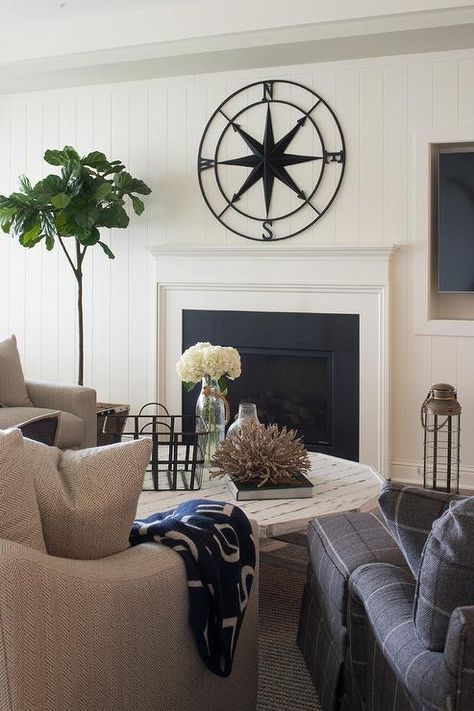 You'll feel right at home in this lovely cottage style living room featuring a wrought iron compass fixed to an ivory shiplap wall above a white fireplace mantel contrasted with a black surround. Decor Over Fireplace, Clock Above Fireplace, Compass Decor, Shiplap Living Room, White Fireplace Mantels, Farmhouse Fireplace Mantels, Cozy Sitting Room, Cottage Style Living Room, Above Fireplace