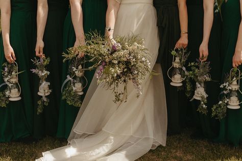 A bride in the center holding her bouquet, and three bridesmaids on either side of her in green floor length dresses holding white Lanterns Nontraditional Bridesmaid Bouquet, Lantern Wedding Bouquets, Unique Bridesmaid Bouquet Ideas, Flowerless Bouquet, Forest Wedding Bridesmaids, Lantern Bouquet, What Can Bridesmaids Carry Instead Of Flowers, Bridesmaids Lanterns Bouquets, Pagan Wedding Bouquet