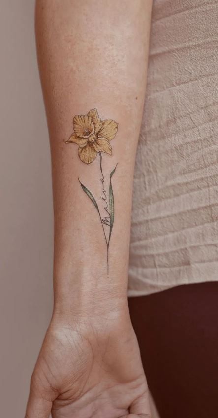 100 Meaningful Daffodil Tattoo Designs - Tattoo Me Now Daffodil Wrist Tattoos For Women, Daffodil With Name Tattoo, Daffodil Tattoo With Name In Stem, Unique Daffodil Tattoo, Single Daffodil Tattoo, Daffodil Memorial Tattoo, Colored Daffodil Tattoo, Daffodil Tattoo Watercolor, Rose Daffodil Tattoo