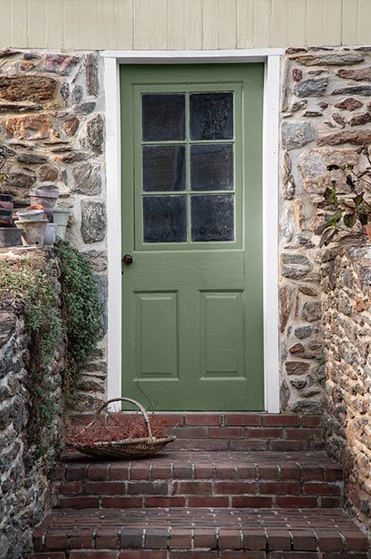 Brick stairs leading up to a green front door surrounded by stacked stone. Yellow Door Green Shutters, Green Front Door Stone House, Front Door Colors With Stone House, Yellow House With Green Door, Dark Gray House With Green Door, Brick House With Painted Front Door, Green Front Door Colors With Red Brick, Green Door Cottage, Green Paint For Front Door