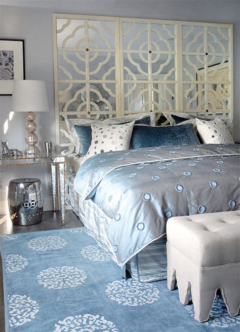 Glam bedroom with gray blue walls paint color, mirrored console table nightstands with gold trim, ivory mirrored quatrefoil pattern floor screen used as headboard, champagne metal lamps, silver garden stools, Madeline Weinrib Atelier Light Blue Mandala Rug and light gray linen tufted ottomans. Blue Gray Bedroom, Blue And White Decor, Blue Painted Walls, Silver Bedroom, Floor Screen, Mirror Headboard, Contemporary Nightstand, Glam Bedroom, Mirrored Console Table