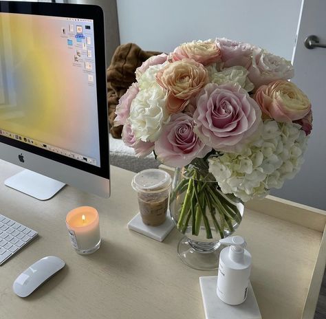 A picture of flowers in a vase sitting on a Woden sleek desk with a apple desk top computer. A candle is lit with a few little skincare bottles. Business Woman Office Working Aesthetic, Flowers On Desk At Work, Office Desk Aesthetic Woman, Desk Top Aesthetic, Office Woman Aesthetic, Desk Job Aesthetic, Office Desk Decor For Work Cubicle Women, Office Desk Decor For Work Cubicle, Business Work Aesthetic