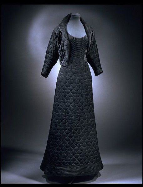 Evening Dress, Matilda Etches, London England: 1947, Quilted silk crêpe lined with silk and cotton. "This cosy evening gown and jacket are quilted in the then popular shell pattern. They were specifically designed for winter evenings in the late 1940s. At this time, coal shortages in Britain after the war made the heating of public places unreliable. Matilda Etches selected fine black silk crepe to create a slimming effect and lined the jacket with an eye-catching vivid purple silk..."