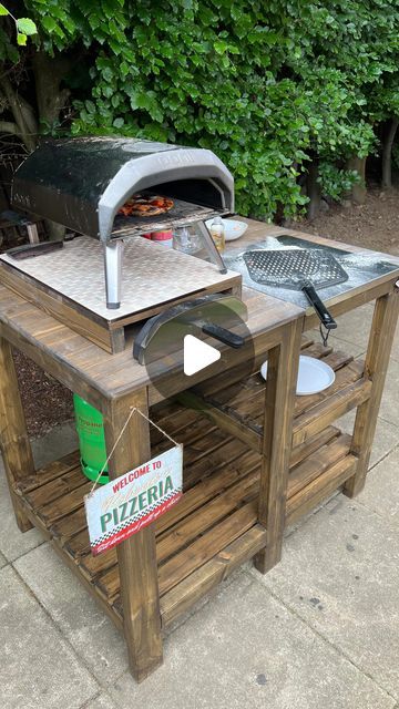 Shade Egun on Instagram: "ad. DIY PIZZA OVEN TABLE 🍕 We wanted to build a stand for our pizza oven so we can make the most of using it over the coming summer but I wanted it to be as simple to build as possible. I bolted the base together to make sure it was really sturdy and added thinner wooden slats for the table top surface and shelves gluing them in place with UniBond No More Nails Waterproof. Perfect because it’s suitable for indoor and outdoor projects and we’re going to be leaving the pizza oven outdoors over the summer! This adhesive sticks to so many absorbent and non-absorbent materials too like brick, MDF, concrete, ceramic so it’s the perfect choice for so many projects.  To personalise it we added some accessories like a beer opener and a ‘Roberto’s Pizzeria’ sign which is j Pizza Outdoor Kitchen, Pizza Oven Set Up, Outdoor Pizza Oven Stand Ideas, Pizza Oven Area, Diy Pizza Oven Table, Diy Ooni Pizza Oven Stand, Ooni Pizza Oven Table, Pizza Oven Table, Pizza Oven Stand