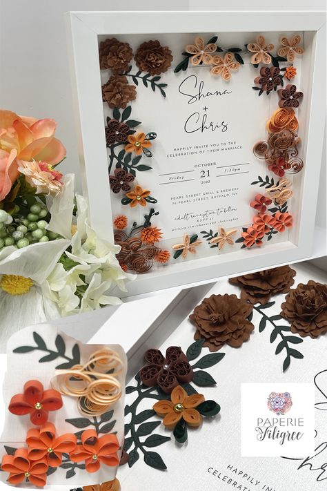 White shadow box displaying a fall wedding invitation keepsake made of fall colored paper flowers that mimic the wedding flowers. There are simple five petal flowers of varying fall colors and many have beads attached to the centers. Machine cut hand formed flowers and leaves are also included and they all surround the wedding invitation beautifully.. Wedding Memory Box Ideas, Terracotta Fall Wedding, Wedding Quilling, Quilling Wedding, Quilling Wall Art, Wedding Invitation Keepsake, Wedding Memory Box, Wedding Gift For Couple, Paper Craft Videos