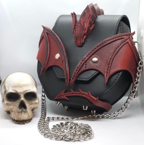 Immerse yourself in refined darkness with this premium dragon handbag in meticulously handcrafted leather. Made from high quality leather including "Crazy Horse". This bag is a unique work with its surprising details and clean lines. The visible stitching adds a striking texture to the workmanship, while the metal chain captures the attention. This unique piece will be an ideal gift for collectors, but also for a nighttime getaway or a day of urban discovery. It can be placed anywhere without wearing out thanks to its high quad rivets. "Crazy Horse" leather is incredibly strong, durable and durable compared to other materials. All its shades of color make it charming. This handbag is the ideal companion to express your individuality with elegance. Color: red and black Dimensions: 20x17x7cm Hand Sewn Bag, Handbag Design Ideas, Fantasy Satchel Leather Bags, Gothic Leather Bags For Halloween, Cyberpunk Bag, Weird Bags, Gothic Leather Bags For Daily Use, Black Leather Gothic Bags, Dragon Fashion