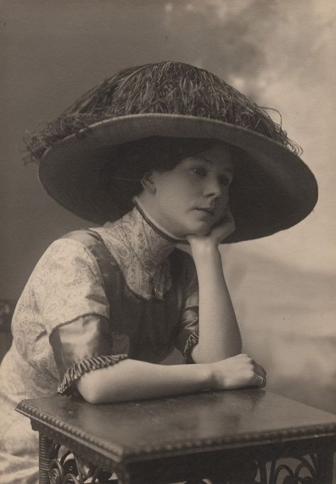 Photographer: Reuben R. Sallows (1855 - 1937)  Description:  Studio portrait of young woman, seated resting chin on left hand with elbow on square table top; right arm rests across table top; wears wide-brimmed hat covered in feathers, short-sleeved patterned dress with satin trim, high neck with lace trim, jewelled necklace; shaded landscape backdrop; writing on back identifies subject Flo Saunders  Object ID : 0385-rrs-ogohc-ph  View additional photographs by Sallows that are held in other ... Arms On Table Pose, Hands On Table Pose, Hand Resting On Chin Reference, Resting Head On Table Pose, Elbow On Table Pose Reference, Hands On Chin Pose, Person Resting Head On Hand Reference, Hands On Table Reference, Resting Head On Hand Pose