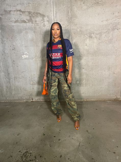 Parking garage outfitinspo, jersey outfit , black girl in braids with cargo pants and heels. Gold jewelry Soccer Jersey Aesthetic Outfit, Women’s Soccer Jersey Outfit, Cargo Pants And Jersey Outfit, Soccer Top Outfit Women, Jersey Outfit Ideas For Black Women, How To Style Soccer Jersey, Jersey Party Outfit Black Women, Soccer Jersey Outfit Women Aesthetic, Soccer Jersey Outfit Women Style