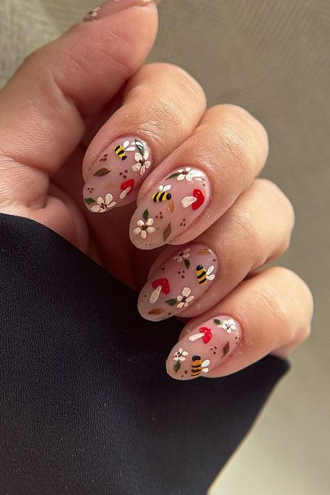 These almond-shaped nails are a whimsical ode to nature. A soft nude base is the perfect canvas for the intricate designs featuring buzzing bees, dainty white flowers, tiny red mushrooms, and subtle green leaves. The playful details bring an enchanting woodland vibe to your fall manicure. Adorable and charming!  // Photo Credit: Instagram @freshsetlancaster Woodland Nails, Mushroom Nail Designs, Nails Mushroom, Trendy Fall Nail Designs, Cottagecore Nails, Autumn Nail Ideas, Mushroom Nails, Strawberry Nails, Oval Shaped Nails