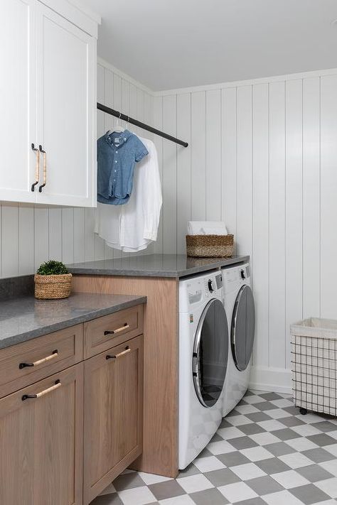 A white front loading washer and dryer sit on white and gray harlequin floor tiles and are enclosed beneath a gray countertop fixed against vertical shiplap trim and under a black drying rod. Grey Washer And Dryer, Shiplap Laundry Room, Cottage Style Mudroom, Ikea Laundry Room Cabinets, Laundry Room Idea, Ikea Laundry Room, Transitional Laundry Room, Laundry Room Countertop, Grey Laundry Rooms