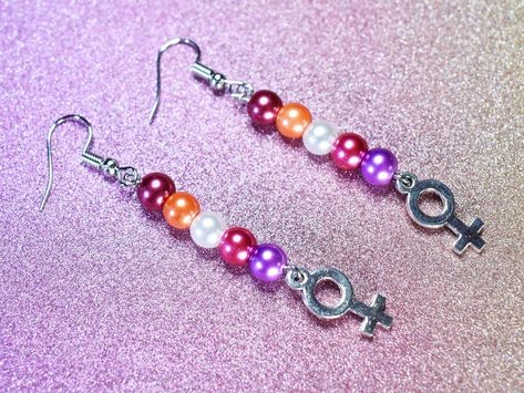 These earrings feature antique silver tone Venus symbols, affixed to eye pins adorned with faux pearls in colours inspired by the Sunset Lesbian Pride Flag. The ear wires are surgical steel alloy, with silicone back fasteners are included. Lesbian Jewelry Fashion, Lesbian Accessories, Sunset Lesbian Flag, Venus Symbol, Pride Jewelry, Lesbian Pride Flag, Pride Stuff, Pride Jewellery, Lesbian Flag