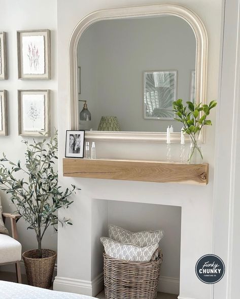 A bedroom wall that is painted white. There is a large white mirror on the wall and below the mirror is a wooden mantel. On the mantel is a vase with green flowers, candles, and a photo frame. Below the mantel is a square hole where a fireplace used to be. Now there is a wicker basket there with two white cushions inside. To the left of the wall you can see a tall plant, and behind that are four matching photos in white frames hung on the back wall. Country Style Bed, Rustic Bedroom Furniture, Wood Mantel, Storage Solutions Bedroom, Cosy Bedroom, Wooden Bedside Table, Scandinavian Bedroom, Wood Mantels, Neutral Bedroom