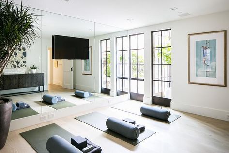 Home yoga room with a TV on floor-to-ceiling mirrors a glass door to the backyard and crisp white walls featuring wall art. Gym Mirror Wall, Zen Yoga Room, Yoga Room Design, Home Gym Mirrors, Home Yoga Room, Home Gym Basement, Media Room Design, Gym Mirrors, Gym Room At Home