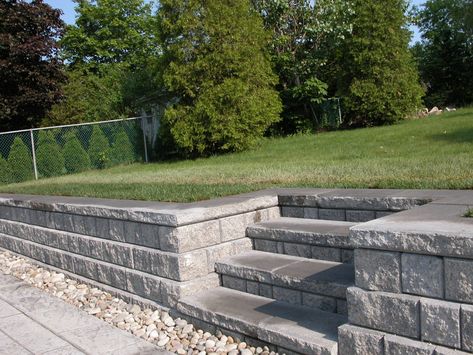 Steps and retaining wall accommodating to levels of patio Retaining Wall Entrance, Diy Retaining Wall With Steps, Versa Lok Retaining Wall, Parking Pad Retaining Wall, Steps In Retaining Wall, Patio With Retaining Wall Ideas, Sunken Patio Retaining Walls, Concrete Patio With Retaining Wall, Deck With Retaining Wall