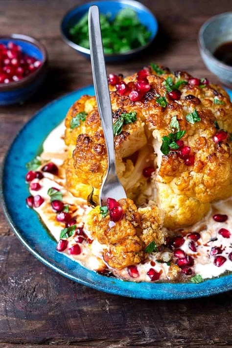 a whole roasted cauliflower with feta and yogurt sauce topped with pomegranate dressing and mint leaves on a plate being cut into by a fork. Mediterranean Veggies, Veggies Roasted, Charred Cauliflower, Appetizer Table, Pomegranate Recipes, Roasted Cauliflower Recipes, The Mediterranean Dish, Cauliflower Dishes, Mediterranean Diet Meal Plan