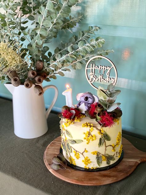 Australian themed 1st birthday party. Beautiful wattle birthday cake complete with gumnuts and koala cake topper. Complemented with Australian native flowers and gumnuts as decorations. May Gibbs Party, Australiana Birthday Party, Australian Native Wedding Cake, Australiana Theme Party, Australian Themed Birthday Party, Australian Cupcake Ideas, Kangaroo Themed Birthday Party, Cake With Native Australian Flowers, Australiana Cake