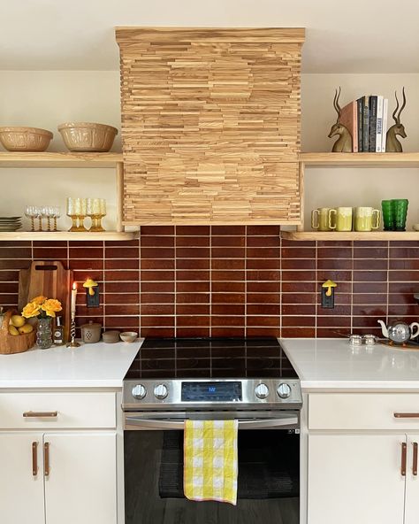 White kitchen with deep red brown tile backsplash, wooden shelves, and decorative stove hood Red Backsplash Kitchen, Brown Tile Backsplash, Brown Kitchen Tiles, Kitchen 80s, Red Kitchen Tiles, 80s Kitchen, Red Backsplash, Kitchen Cost, Brown Tile