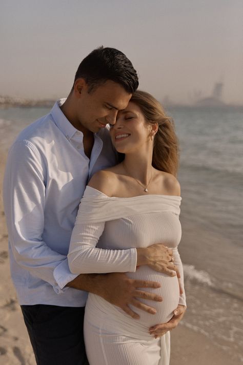 Expectant couple embracing on the beach at sunset, with the man holding the woman's belly, both sharing a moment of connection in a serene seaside environment. Pregnancy Photoshoot Ideas Couple, Beach Pregnancy Photoshoot, Beach Maternity Photos Couples, Pregnancy Photoshoot Beach, Mermaid Shoot, Beach Maternity Photoshoot, Maternity Photography Beach, Maternity Photoshoot Ideas, Expectant Father