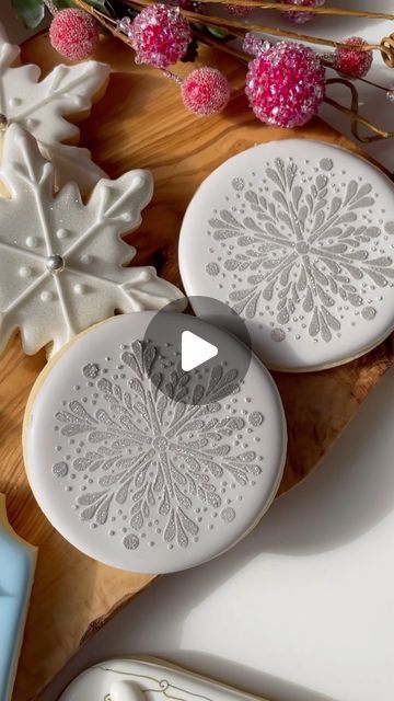 Annamaria Valentino || Mary on Instagram: "A glittery snowflake made simple using a stencil and edible sparkle dust 💫💫 make sure your royal icing base is completely dry before stenciling. Use a medium to stiff consistency icing to scrape across the stencil, then finish with some edible sparkle dust and lift the holder to reveal a perfect snowflake ❄️ You can find all of these tools/supplies on my website 💫💫💫💫. I will list them all below : ❄️Pretty snowflake stencil 🖤Super Black Fondust (used a touch of Colourant for this grey colour) 💫Nu Silver edible sparkle dust ❄️The sweet stencil holder- an amazing tool that gives THE PERFECT stenciling every single time! Comment below and follow for more ! 💫 #emmassweets #cookiedecorating #cookoedecoratingvideo #cookiedecoratingsupplies #cook Stenciled Cookies Royal Icing, Royal Icing Stencils, Christmas Cookie Icing Designs, Stencil Cookies Royal Icing, Royal Icing Tools, Elegant Birthday Cookies Decorated, Snow Globe Christmas Cookies, Snowflake Decorated Sugar Cookies, Silver Royal Icing