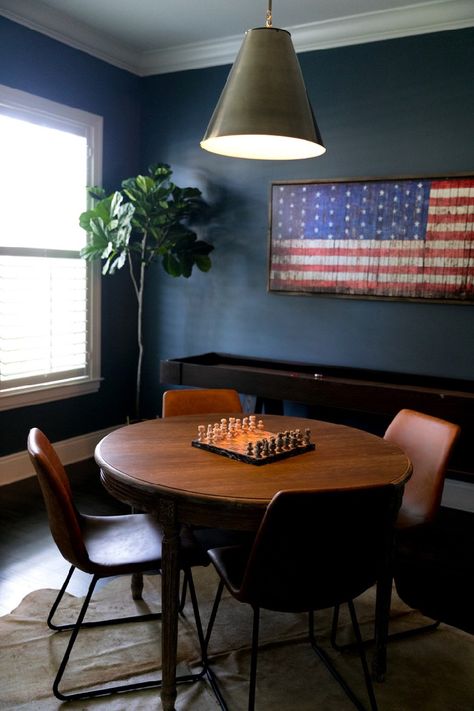 A moody masculine game room with game table, dark blue walls, shuffleboard table and leather and rawhide textures #gameroom #recroom #mancave Family Game Room Table, Round Game Table And Chairs, Game Table In Basement, Card Table Game Room, Game Tables In Basement, Elegant Game Room Ideas, Round Table Game Room, Game Table Room, Basement Table And Chairs