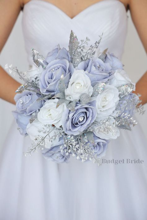 This magnificent rounded brides’ bouquet is crafted using dusty lavender and white roses each embellished with a jewel center of the highest quality. This cheerful and bright bouquet is sure to leave a lasting impression. The shimmery silver glitter accents in this collection, create a bright and dazzling arrangement that is sure to turn heads. With a mixture of silver accents this bouquet is sure to make a statement. All of our bouquets are a wonderful option for destination weddings, as they c Periwinkle And Grey Wedding, Cinderella Themed Wedding Dress, Disney Wedding Bouquet, Lavender And White Roses, Beautiful Wedding Bouquets, Simple Boutonniere, Cinderella Wedding Theme, Fake Wedding Flowers, Bright Bouquet