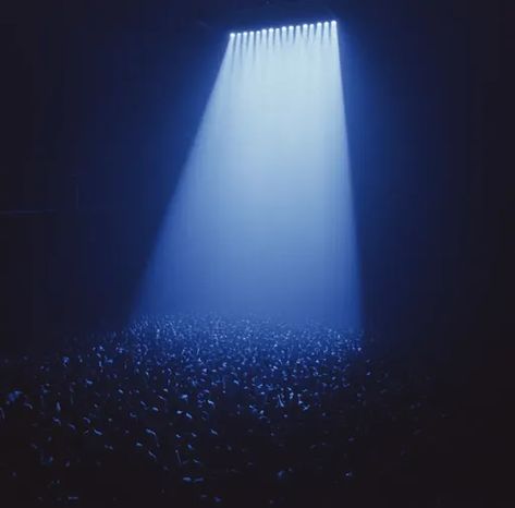 ↑↑↑ Larger size on website 🔸 A large crowd of people are gathered in a dark, dimly lit space. A single spotlight shines down from Single Spotlight, Crowd Of People, Large Crowd