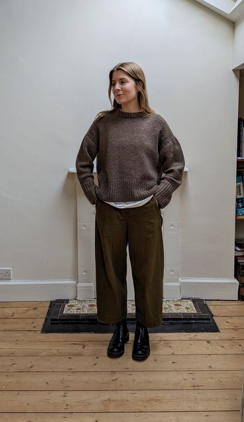 A woman stands in front of a fireplace. She wears a thick brown wool jumper over a white T-shirt, with khaki barrel-leg trousers and black boots. Brown Jumper Outfit, Trousers Outfit, Brown Jumper, Knitwear Outfit, Trouser Outfit, Jumper Outfit, Concept Clothing, Granny Chic, Wool Jumper