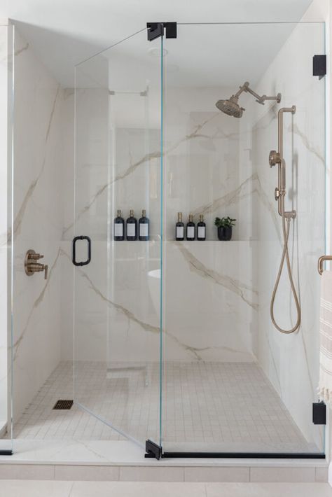 Large walk-in shower, seamlessly clad in porcelain stone slabs. The warm veining of the Calacatta Oro pattern highlights the gold tones of the plumbing fixtures. Matte black hardware on the shower glass creates an interesting mix against the gold plumbing fixtures. Frameless Shower Glass Door Ideas, Quartz Shower Wall, Custom Shower Ideas, Gold Plumbing Fixtures, Granite Shower, Primary Bathroom Remodel, Porcelain Slab, Glass Shower Doors Frameless, Shower Glass