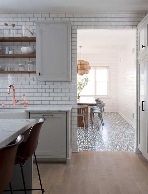 Light gray kitchen accented with gray wash wood floors boasts light gray shaker cabinets donning oil rubbed bronze hardware and a white marble countertop holding a farmhouse sink with a copper gooseneck faucet beneath stacked wooden shelves flanked by gray upper cabinets mounted on a white subway tile backsplash contrasted with dark grout. Gray Wood Tile Flooring, Grey Wood Tile, Light Grey Kitchens, Серая Кухня, Wood Floor Kitchen, Terrazzo Tile, Amazing Kitchen, Kitchen Transformation, Kitchen White