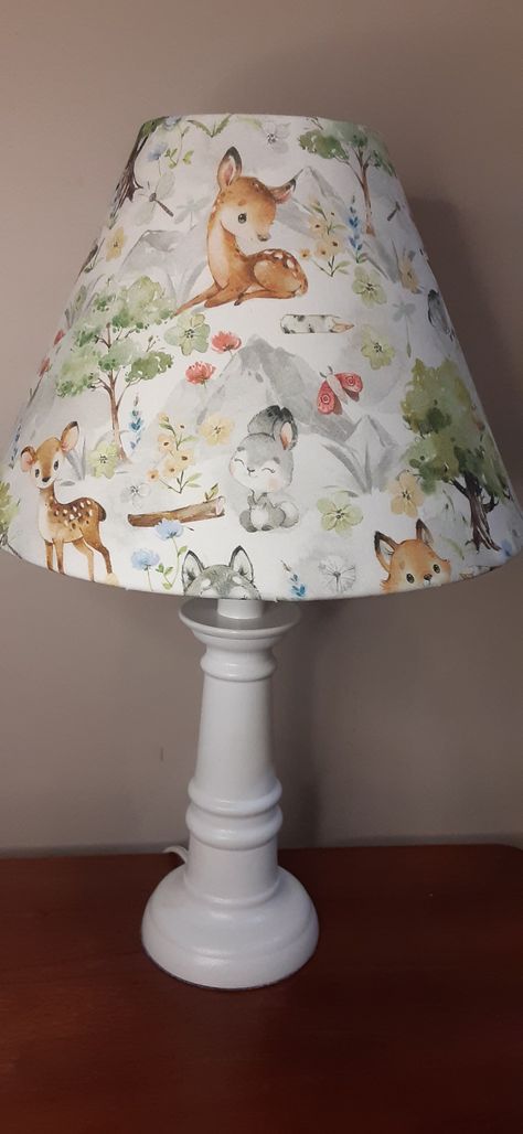 This adorable Nursery lamp features a forest Woodland theme depicting bunnies, foxes, deer, badgers, and beavers in a woodland setting with mountains in the background. This is truly a delightful print in soft watercolors. The shade fits on any lamp base, sitting on the socket above the light bulb on a suspended ring. The shade itself measures 7 and 1/4 in Long by 10 inches wide and fits a base up to 12 in in height. The shade can be purchased alone, or with the lamp base. The assembled lamp offered stands 15 and a half inches tall as the base itself is 11 and 1/4 in tall. The hand painted and sealed base is offered in sage, white, or light gray. This Unique Piece is both decorative and functional and would look perfect in a baby's nursery or a child's bedroom or playroom. Nursery Lamp Shade, Forest Nursery Ideas, Deer Bedroom, Woodland Forest Nursery, Woodland Bedroom Decor, Mushroom Nursery, Base Sitting, Woodland Creatures Nursery, Baby Lamp