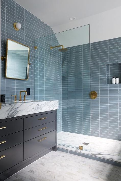 Bathroom features shower with stacked blue glass tiles, a blue tiled shower niche, aged brass shower kit, gray marble hexagon floor tiles and a glass partition next to a dark blue washstand topped in marble under a rectangular pivot mirror. Blue Shower Tile, Blue Glass Tile, Blue Bathroom Tile, Marble Bathtub, Shower Fixtures, Transitional Bathroom, Blue Tile, Shower Niche, Blue Bathroom