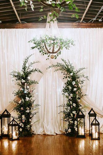 wedding altar decoration background of white cloth the altar of greenery with white flowers is surrounded by lanterns janelle sutton via instagram Wedding Alter Decorations, Winter Wedding Arch, Wedding Altar Decorations, Winter Ceremony, Indoor Wedding Ceremony, Wedding Altar, Wedding Alters, Altar Flowers, Wedding Altars