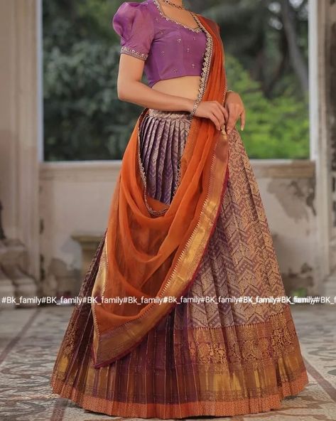 Do you need a beautiful and unique half saree for your next special occasion? Look no further than this lavender and orange Banarasi Silk lehenga! This gorgeous blouse features a collared V-neckline and puff sleeves with lace detailing on the yoke and sleeves, and the fabric used for it is golden tissue silk. The back of this dress is surely a head-to-turn pattern. It is paired with an organza silk-bordered dupatta. Whether you’re attending a wedding, a party, or a family occasion, this Banar... Lavender Half Saree, Lavender And Orange, Trendy Outfits Indian, Outfits Indian, Gorgeous Blouses, Silk Lehenga, Half Saree, Do You Need, Puff Sleeves