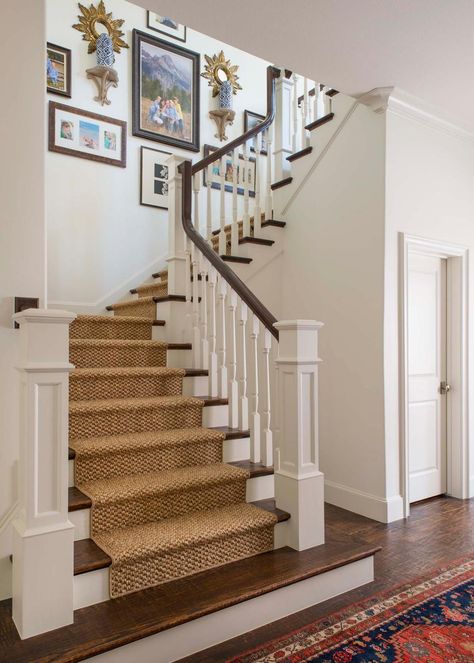 A textured carpet runner gives a burlap look to the top of these stairs for a subtle southern influence in the design. White newel posts create an entrance frame then white balusters and a deep wood hand rail line the rest of the design. Family photos and mounted candle displays add personality and color to the white wall space. Carpet Lined Stairs, Colonial Stair Runner, Southern Staircase, Add Railing To Stairs, Stair Runner Carpet Top Of Stairs, Traditional Stair Runner, Stair Runners Ideas, Colonial Staircase, White Staircase