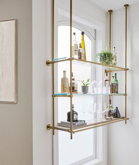 Keeping it light, bright, and airy with this delicate window-front wall + ceiling mounted shelving unit. Warm brass posts support two glass upper shelves and one bottom wood shelf, perfect for displaying those special pieces. #homedecorideas #interiordesignideas #kitchenideas #shelvingideas #kitchenshelving (Photo by K Interiors/ Kristen Pena) Shelves For Bar, French Bistro Shelves, Bistro Shelves, Bistro Shelving, Brass Shelves, Kitchen Custom, Luxury Materials, Bar Shelves, Loft Lighting