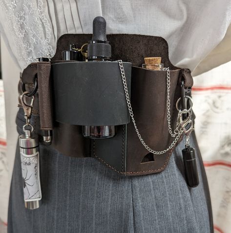 Leather belt sheath with pockets and rings to hold vials, bottles, and tools. All included accessories have chains and clasps which are available in bronze or silver. Included: - Leather belt sheath with center pass through loop on back for stability.  For pockets with no bottom support, I've added chains and clasps so bottles and vials can attach to a ring or hook. - 1 large (4") amber glass dropper bottle - 2 aluminum vials with screw tops(with rubber gaskets) - one black, one silver.  These v Utility Belt Aesthetic, Fantasy Belt Pouch, Alchemist Accessories, Alchemy Belt, Ren Faire Witch, Ren Faire Accessories, Witch Belt, Rogue Accessories, Belt With Pouches