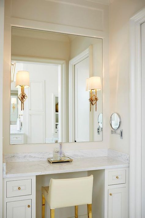 Lovely white and ivory bathroom features an ivory leather stool on gold legs placed at a white built-in makeup-vanity accented with brass hardware and topped with a white marble countertop. Makeup Table In Closet, Makeup Vanity Built In, Built In Bedroom, Built In Makeup Vanity, Bathroom Vanity Stool, Vanity Nook, Vanity In Bedroom, Makeup Vanity In Bathroom, Vanity In Bathroom