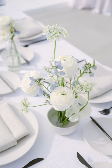 Get inspired by this elegantly set table, perfect for bridal shower ideas! The minimalist floral arrangement with pristine white ranunculus and delicate blue sprigs complements the crisp white plates and linen napkins. 🌸✨ The modern black-handled knives add a chic touch to this tranquil setup. Check out more 🌿 #weddingcenterpieces #bridalshower #wedding #beachwedding #tablescapeideas Coastal Wedding Centerpieces, Boho Table Setting, Bud Vases Wedding, Pale Blue Flowers, Floral Table Setting, Blue Flower Arrangements, Blue Wedding Receptions, Pale Blue Wedding, Blue Table Settings