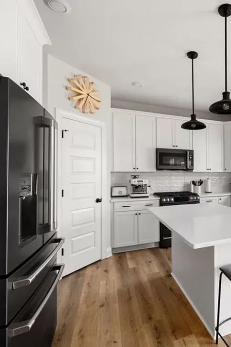 This stunning kitchen features a timeless design with white cabinets, dark stainless steel appliances, and sleek white quartz countertops. The light hardwood floors add warmth and brightness to the space. This is a beautiful example of a kitchen that is both stylish and functional. #whitekitchen #darkaccents #quartzcountertops #lightwoodfloors #timelessdesign #kitcheninspiration #interiordesign #homedecor #dreamkitchen #kitchendesign #homerenovation #kitchenmakeover #modernkitchen #luxurykitche Black Kitchen With White Appliances, Dark Stainless Steel Appliances, White Cabinets With Black Appliances, White Appliances In Kitchen Ideas, White Kitchen With Black Appliances, White Cabinets With Black Hardware, White Kitchen Black Appliances, White Cabinets Black Appliances, Kitchen Island Inspiration