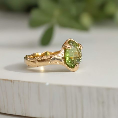 A beautifully handcrafted Peridot engagement ring, uniquely made with wax and cast in solid 14k gold. Its textured band lends a rustic charm to the elegant green stone, captured in a mesmerizing light play. This August birthstone ring is more than just jewelry—it's a poetic expression of individuality and lasting love, perfectly embodying your unique story. Available in sterling silver or solid 14k gold. Engagement Rings Natural Stone, Light Green Ring, Weird Wedding Rings, Rings Engagement Unique, Ethereal Engagement Ring, Peridot Ring Engagement, Organic Engagement Ring, August Jewelry, Green Wedding Ring