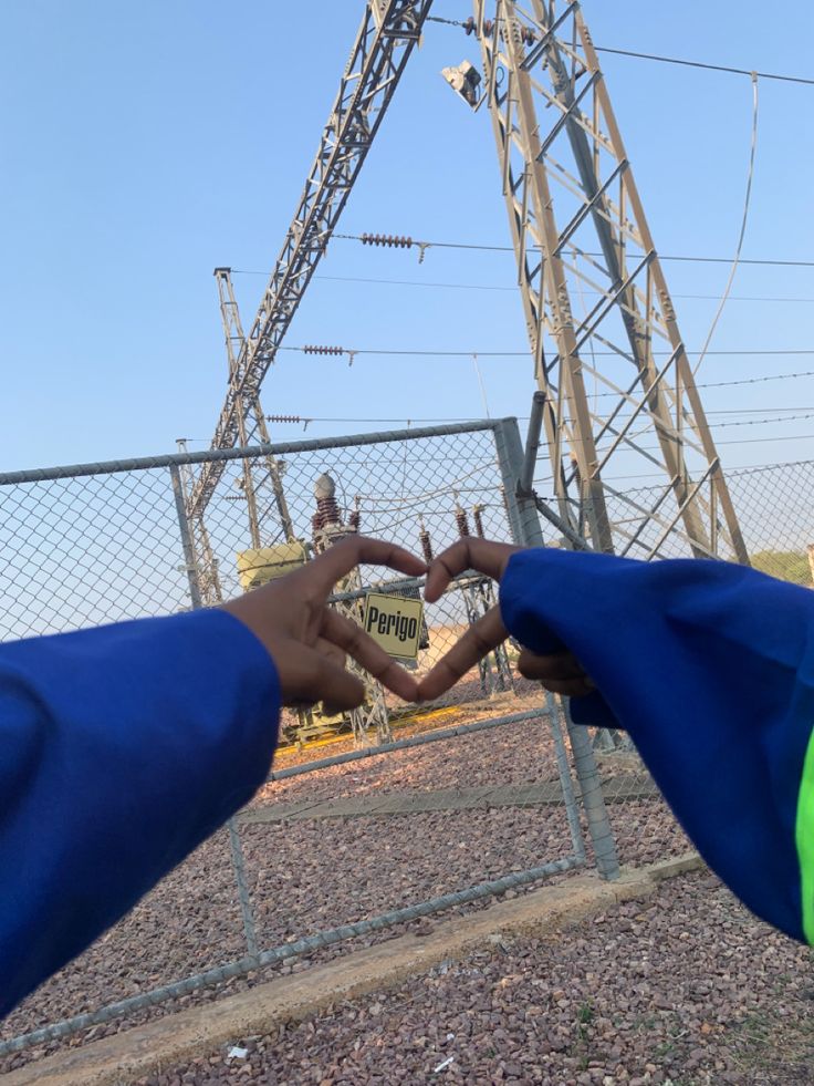 two hands making a heart with their fingers in front of an electric power line tower