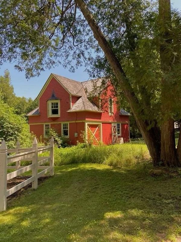 a red house with a white fence in front of it and trees on the other side