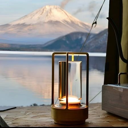 a lantern sitting on top of a wooden table next to a lake with a mountain in the background