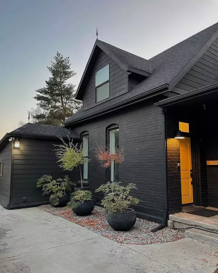 a black house with two large planters in the front yard and yellow doors on each side