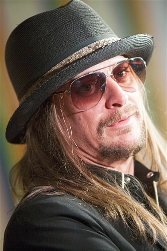 a man with long hair wearing a black hat and sunglasses looking off to the side