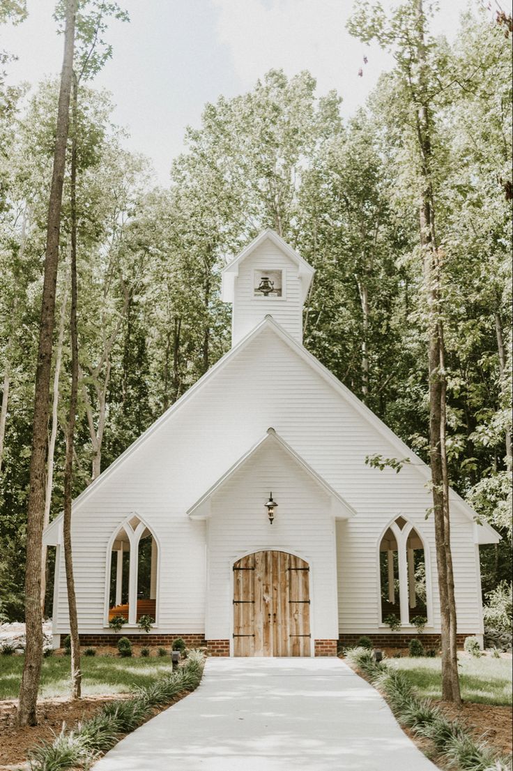 a white church surrounded by trees and greenery is featured in this wedding photo from the front